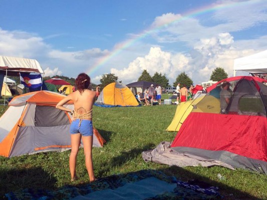 photo of tents on the grass with blue sky, puffy clouds, and a bright rainbow