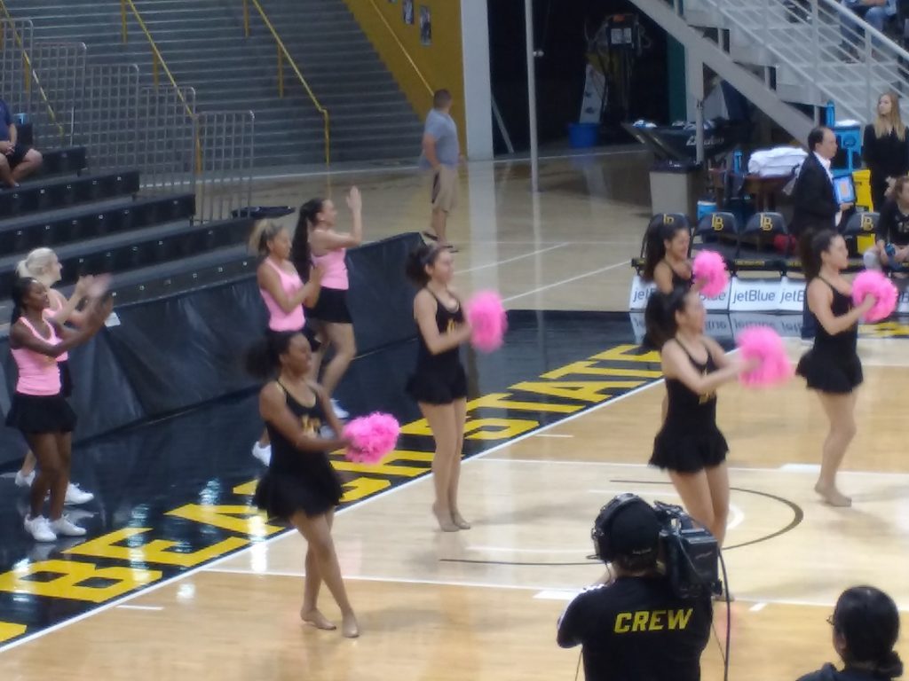 Long Beach State dance team on the court inside The Pyramid and using pink pom-poms for Breast Cancer Awareness night