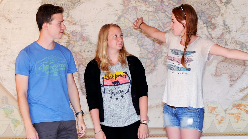 Christof Heck, Sarah Weber & Paulina Smigalski standing in front of a large world map