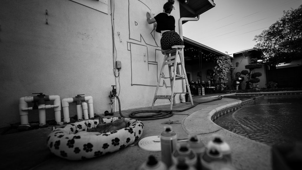 Tiki Brown supervising (sleeping) in a basket surrounded by Montana 94 paint cans as Merijein Saperas paints a "RULA" mural.