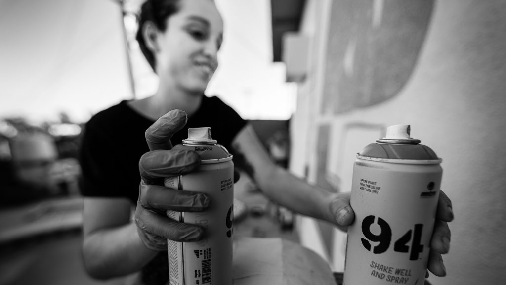 Merijein Saperas working with paint for her "RULA mural" on the Tikiwood veranda at Runaway University, Los Angeles.