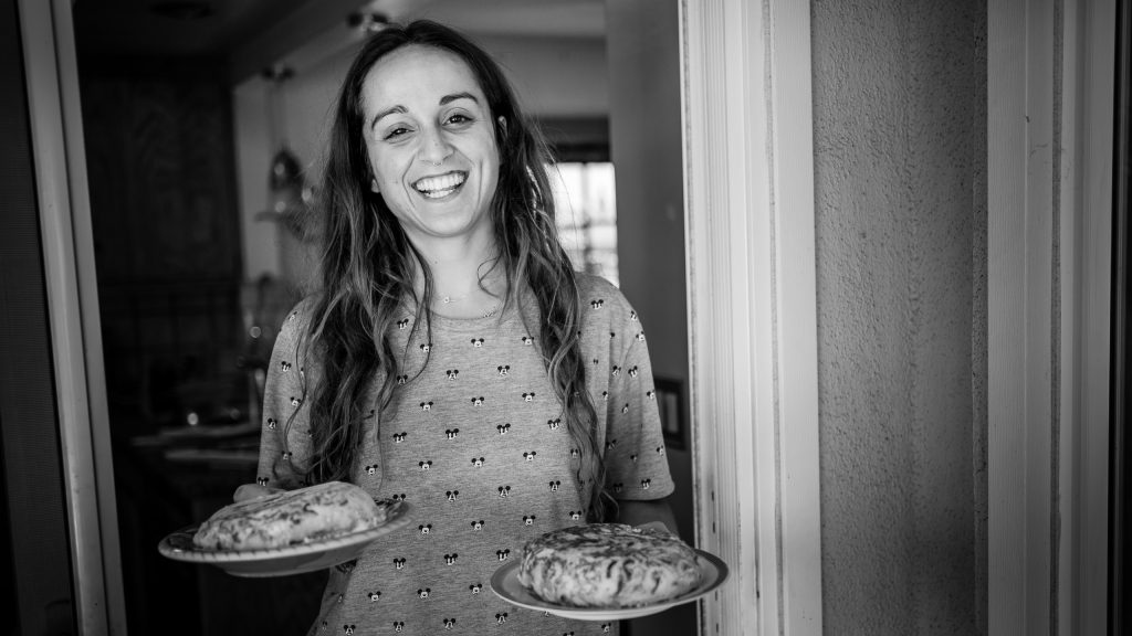 Meri stepping out of the kitchen and into the veranda dining area with two large plates of tortilla de patatas