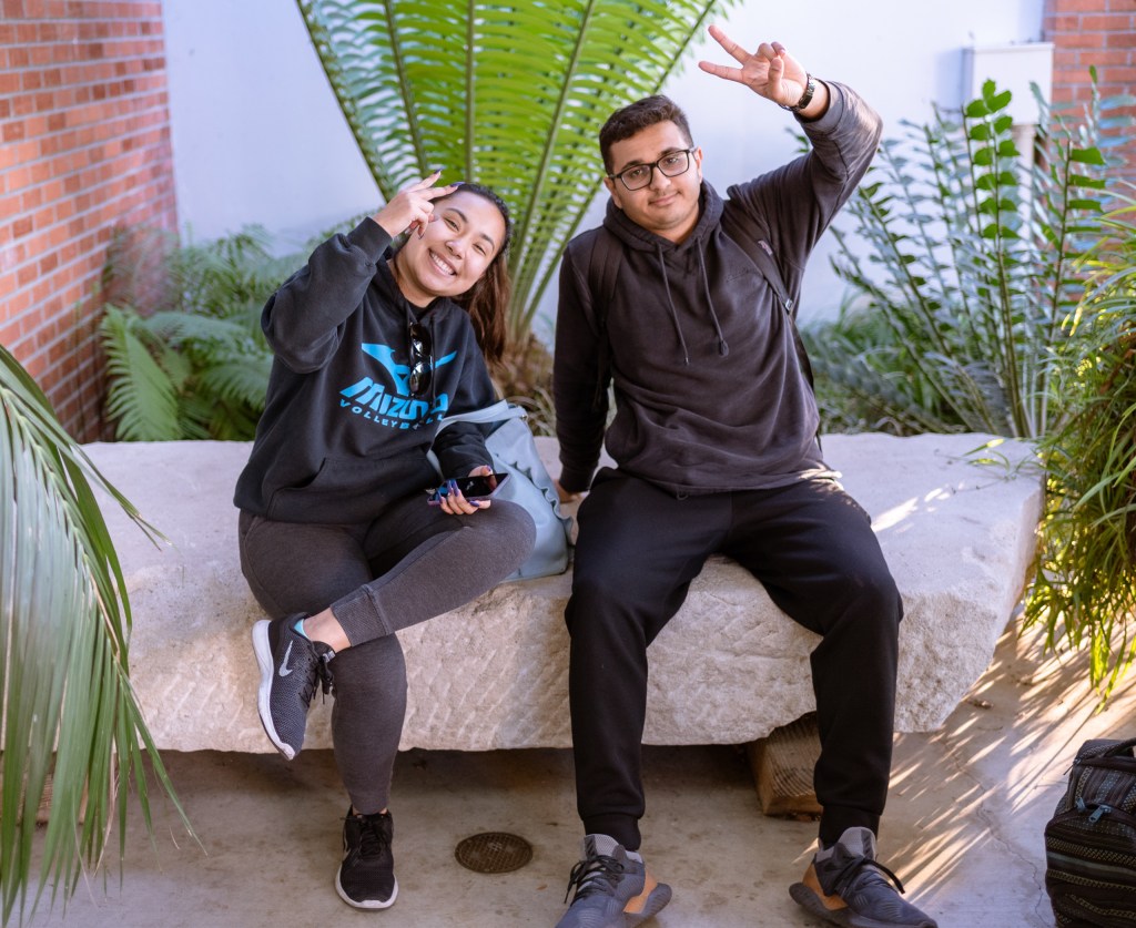 2 students sitting on a large stone in the Art Gallery Courtyard at Long Beach State University.