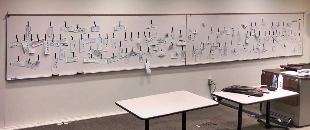 over 100 Scantron 882-E forms taped to a 40-foot-wide white board. Each scantron form is used as a canvas or drawing paper on which each artist has created a unique and personal graphic or image