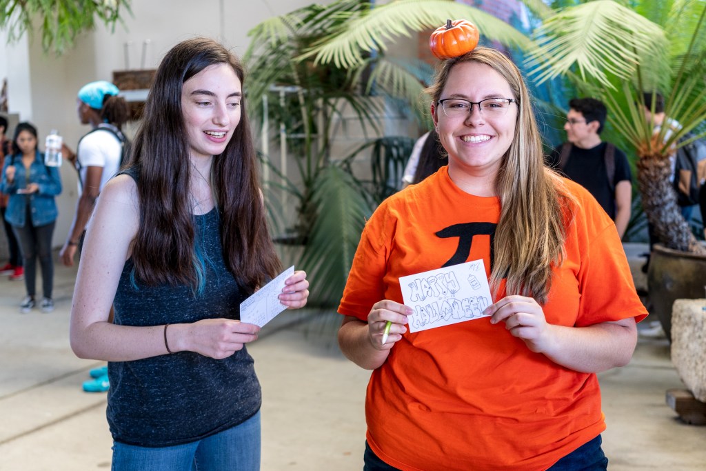 Eleanor Meyer & Hope Kindred in the School of Art Gallery Courtyard at Long Beach State University. Hope Kindred wears a small pumpkin on her head, and a t-shirt with a "pi" symbol on it... "pumpkin pie"