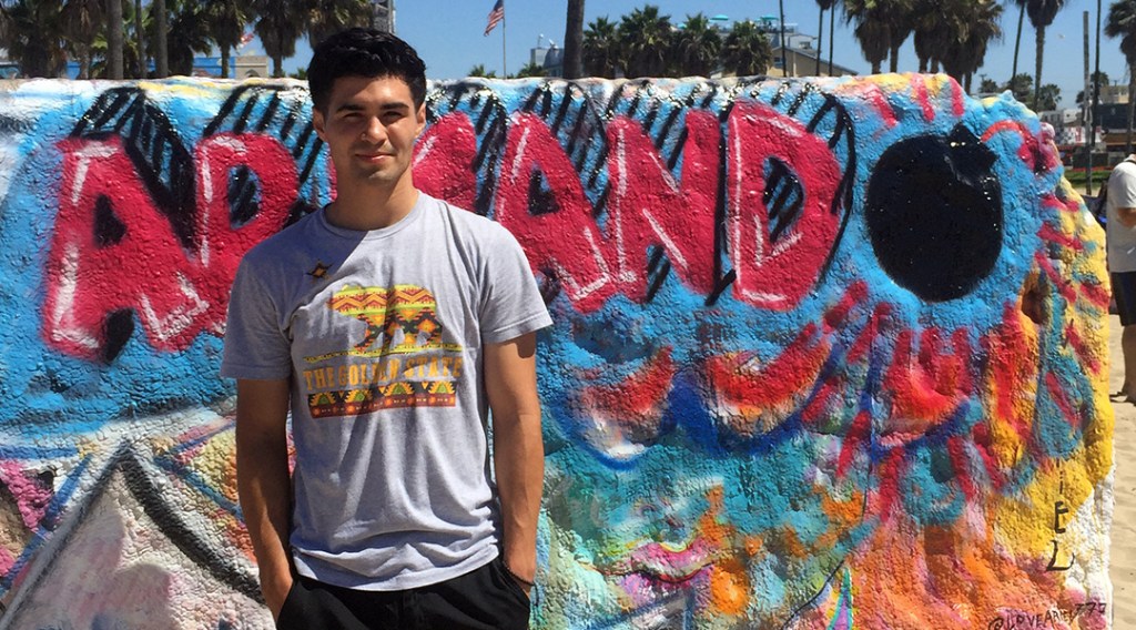 Armando de la Mora standing in front of his name on the Venice Beach Art Walls. The "o" in "Armando" is a round, black, bomb with a fuse