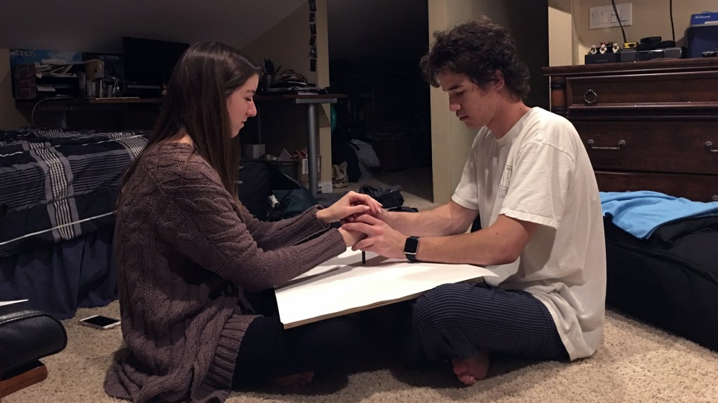 Elizabeth Moledo and her boyfriend Aaron making an Automatic Drawing by facing each other, holding their hands on a pencil over a sheet of drawing paper between them, and letting the pencil go where it will