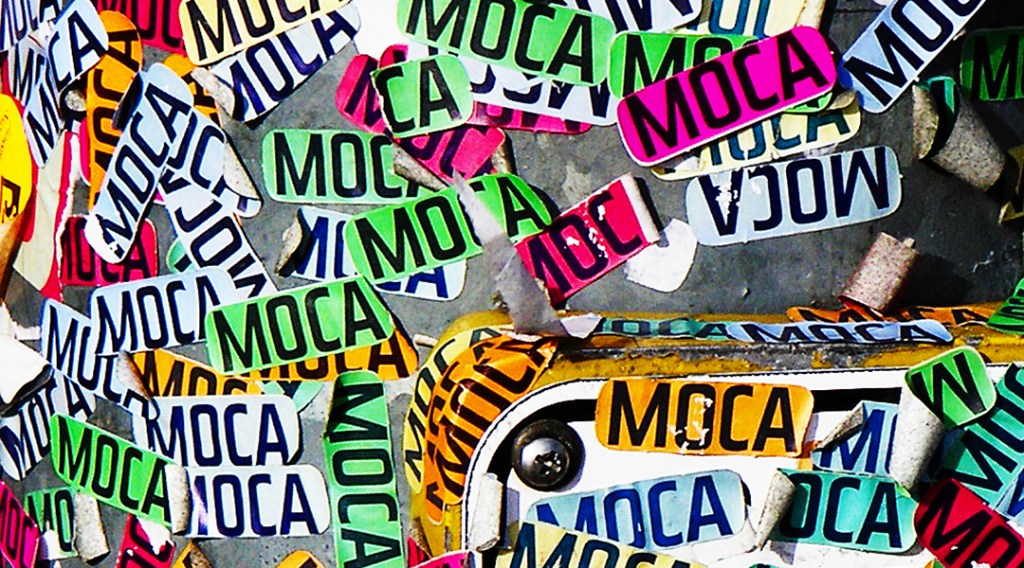 dozens of "MOCA" stickers on a street pole