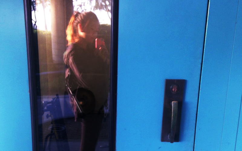 a young woman's reflection in the window as she looks into a music rehearsal room that she no longer has access to