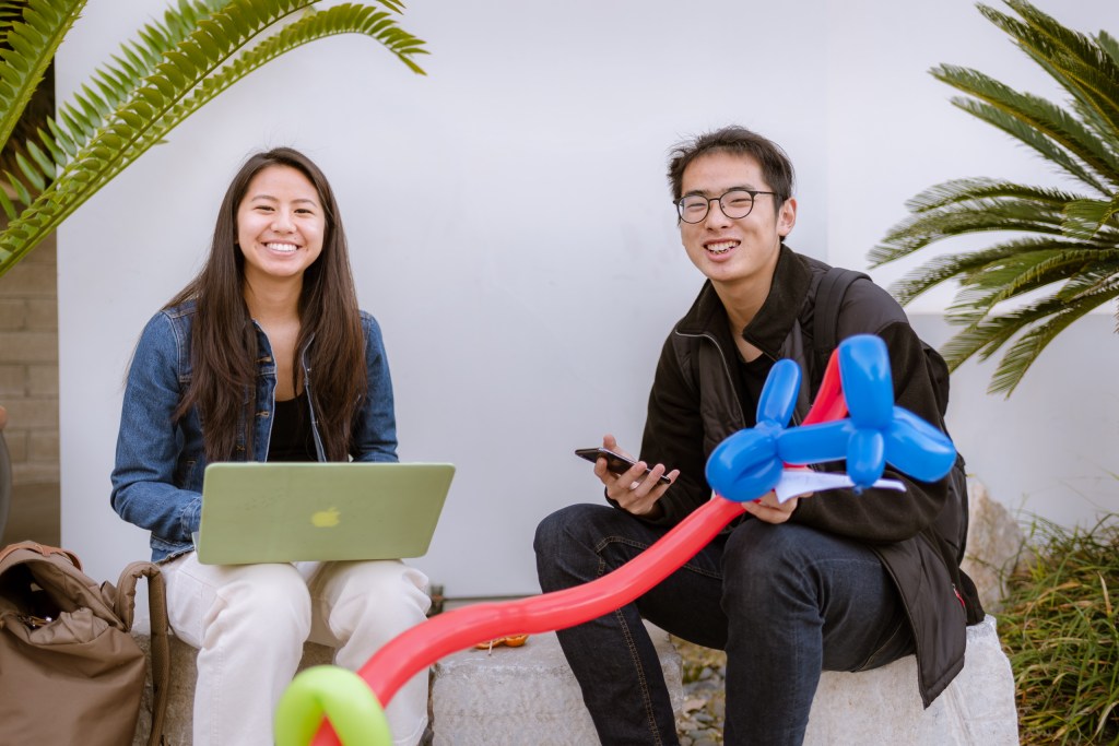 2 students sitting on a large stone in the Art Gallery Courtyard at Long Beach State University.