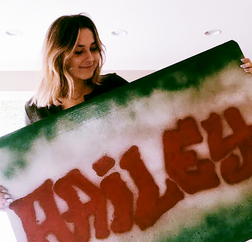 nursing student Hailey Hairrell holding a large board with the name "Hailey" spray painted on it